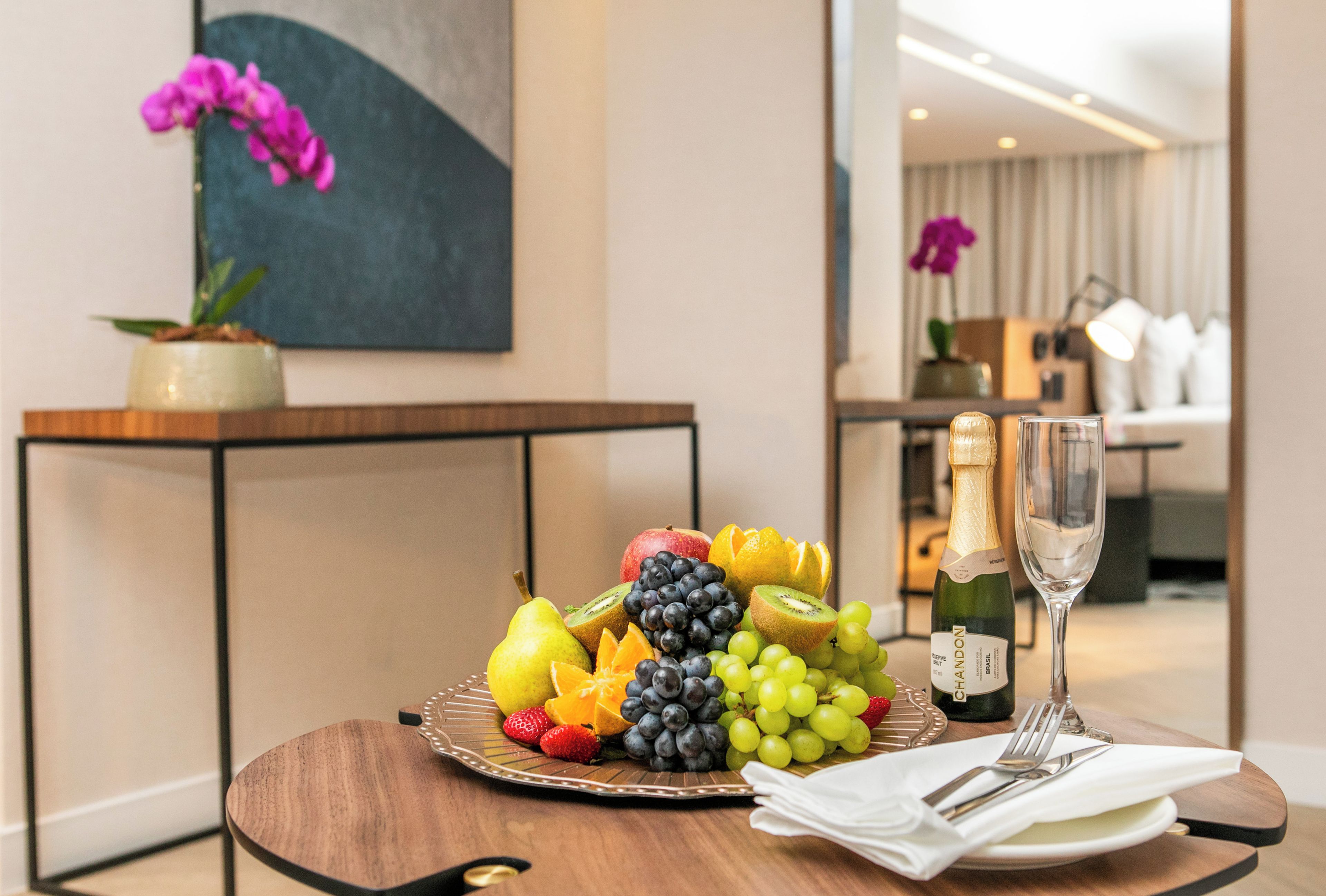 A table with a fruit platter, two champagne bottles, and a glass of champagne.