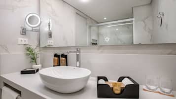 A modern bathroom with a large white sink, a mirror with a ring light, a potted plant, and toiletries on the counter.