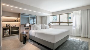 A modern hotel room with a large bed, a small desk, a mirror, and a view of the city through large windows. - Melia Brasil 21 (Brasília)