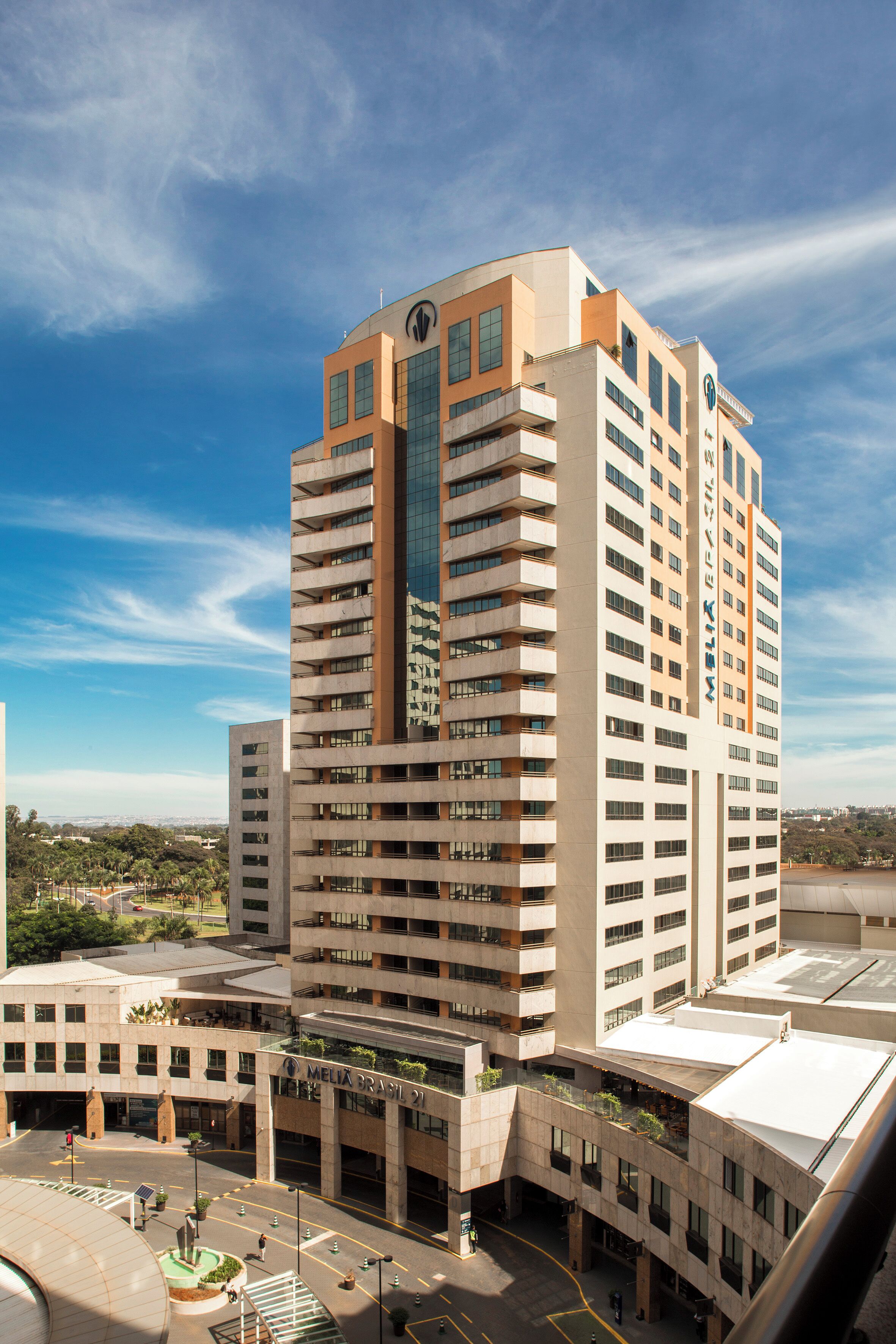A high-rise hotel with multiple floors, a prominent logo on the top, and a parking area in front.