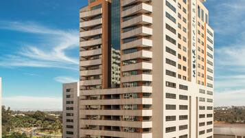 A high-rise hotel with multiple floors, a prominent logo on the top, and a parking area in front.