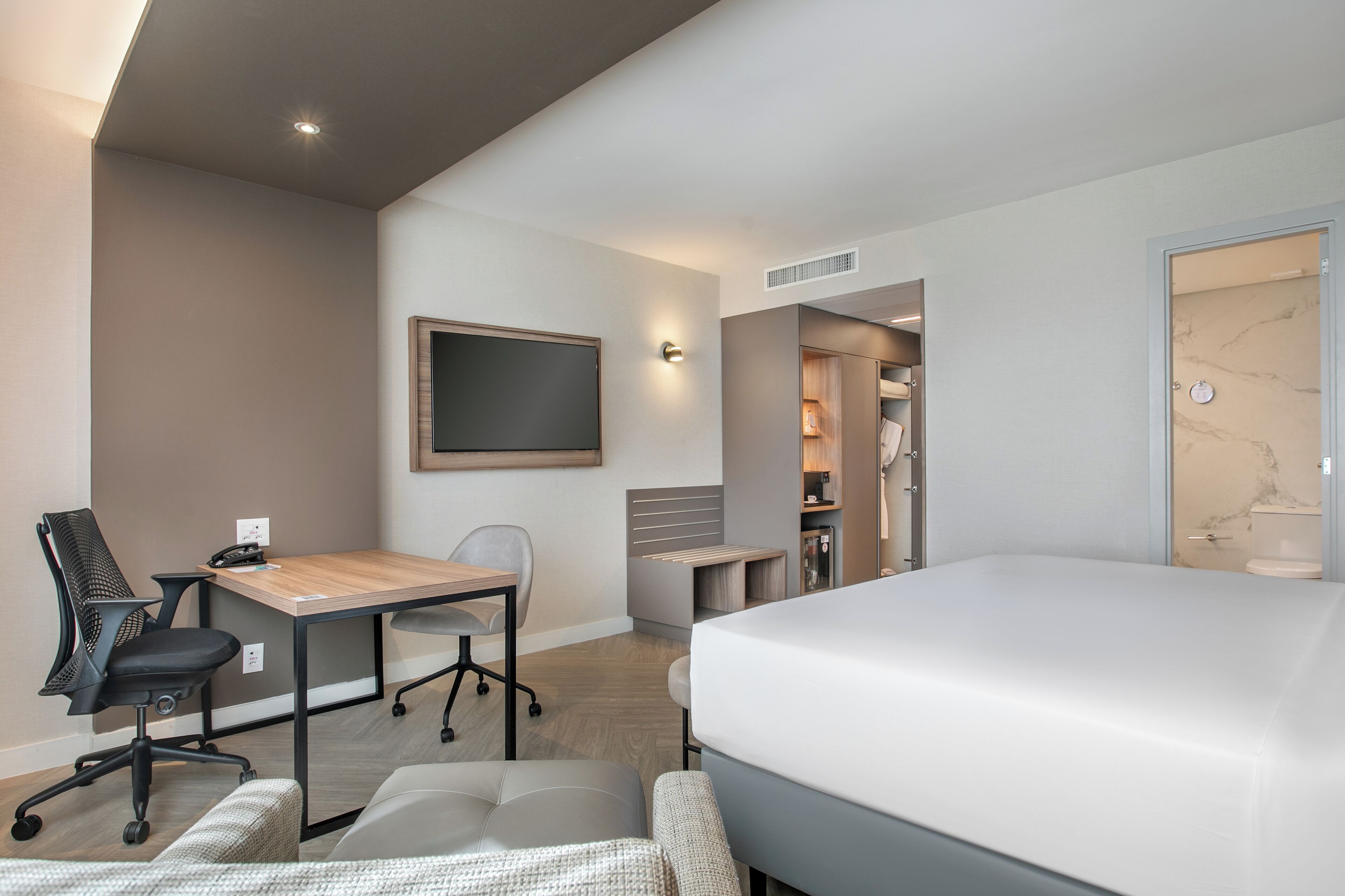 A modern hotel room with a bed, desk, office chair, and a walk-in closet.