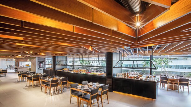 A spacious dining area with multiple tables and chairs, a buffet counter, and large windows offering views of the city. - Melia Brasil 21 (Brasília)