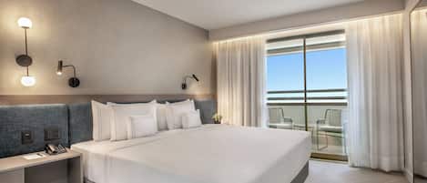 A modern hotel room with a large bed, bedside tables, a desk, and a balcony with a view.