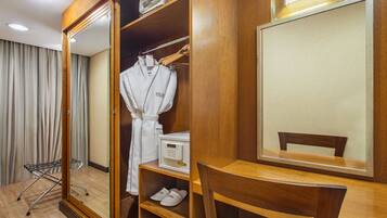 A hotel room with a wooden wardrobe, a mirror, a wooden table, and a chair.