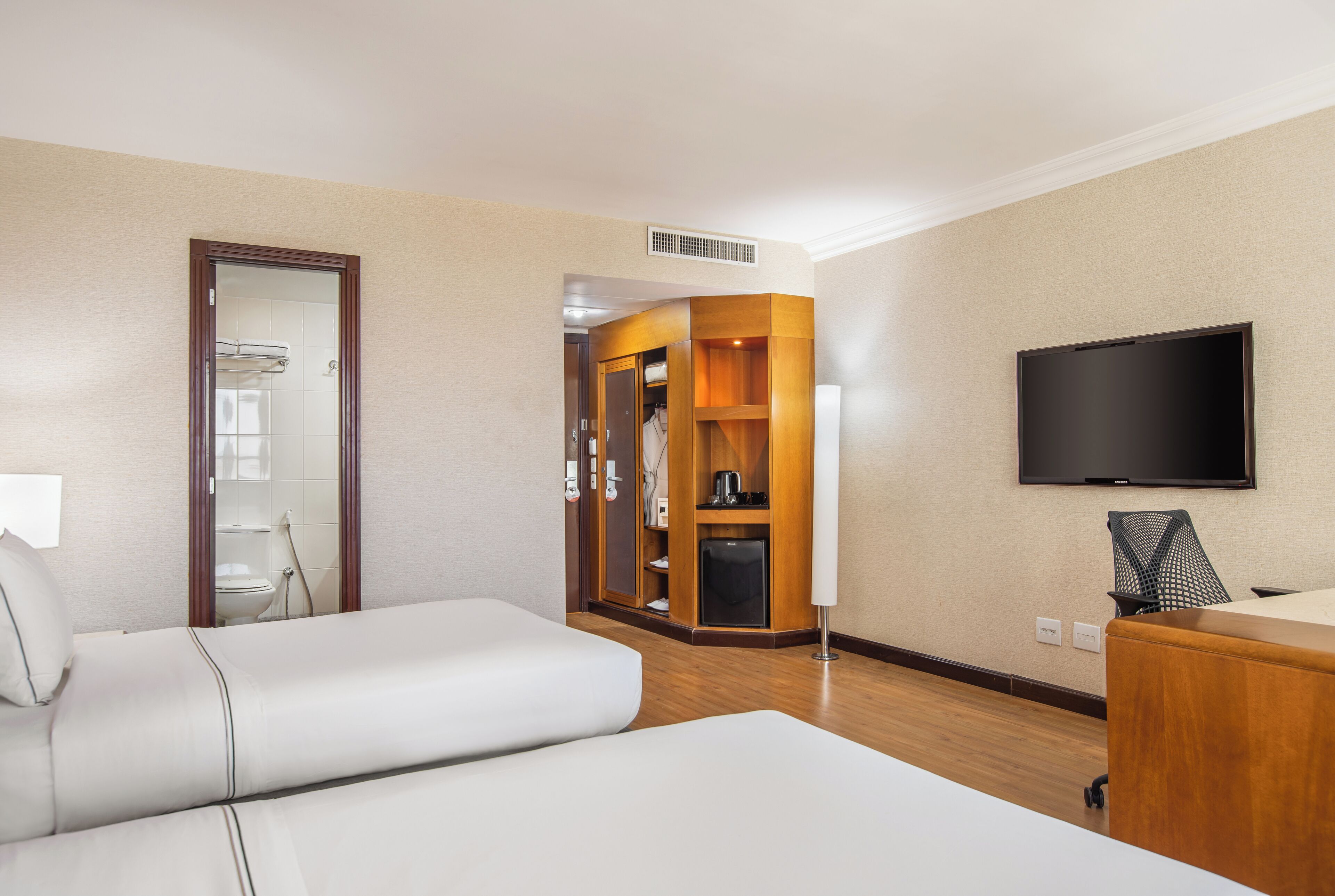Habitación de hotel con cama, televisión, armario y baño visible a través de una puerta.