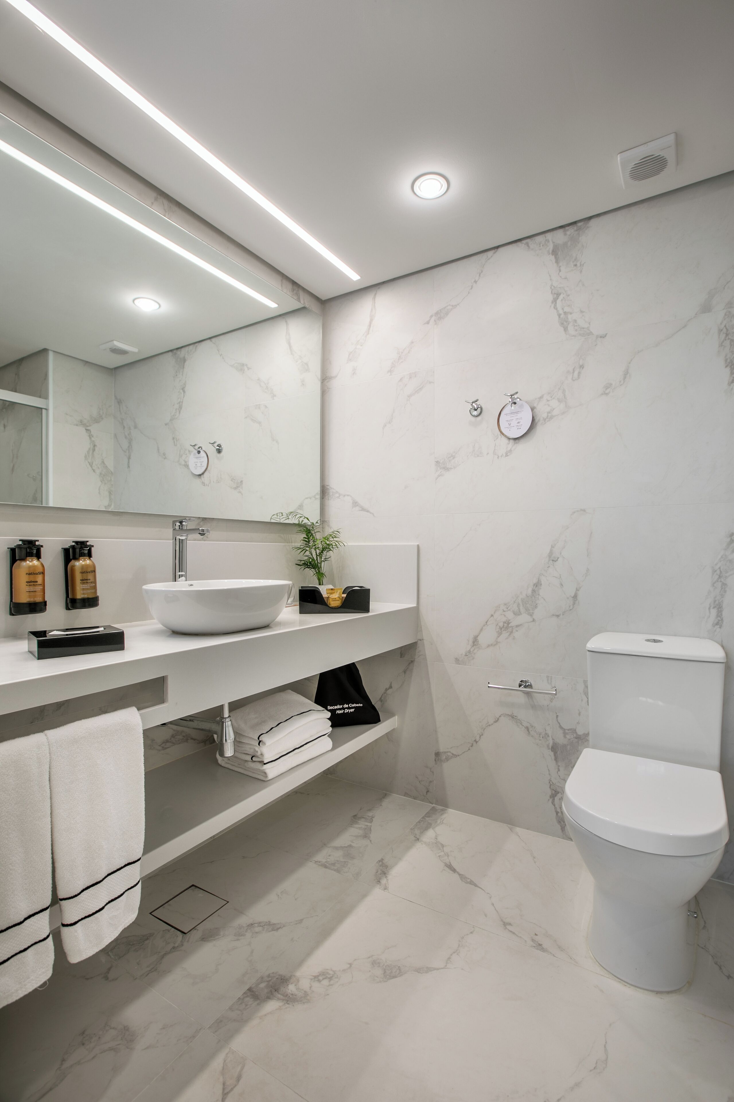 Un baño moderno con un lavamanos blanco, paredes de mármol y un inodoro.