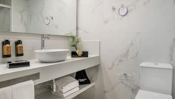 Un baño moderno con un lavamanos blanco, paredes de mármol y un inodoro.