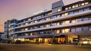 Un hotel de varios pisos con diseño moderno, que cuenta con balcones en cada planta y una entrada destacada con puertas de vidrio.