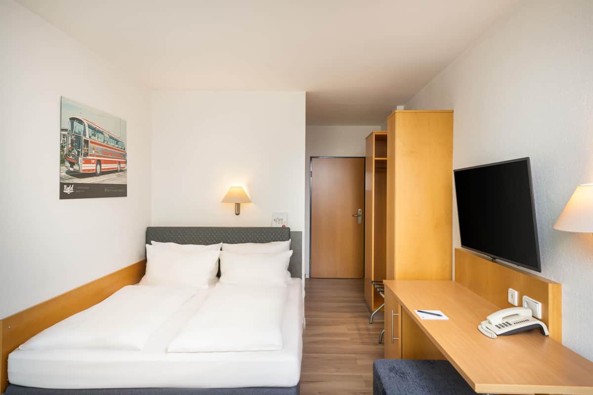 A hotel room with a bed, bedside lamps, a desk with a telephone, a television, and a wardrobe.