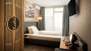 Una habitación de hotel con una cama, un escritorio con teléfono, una lámpara y un televisor montado en la pared.