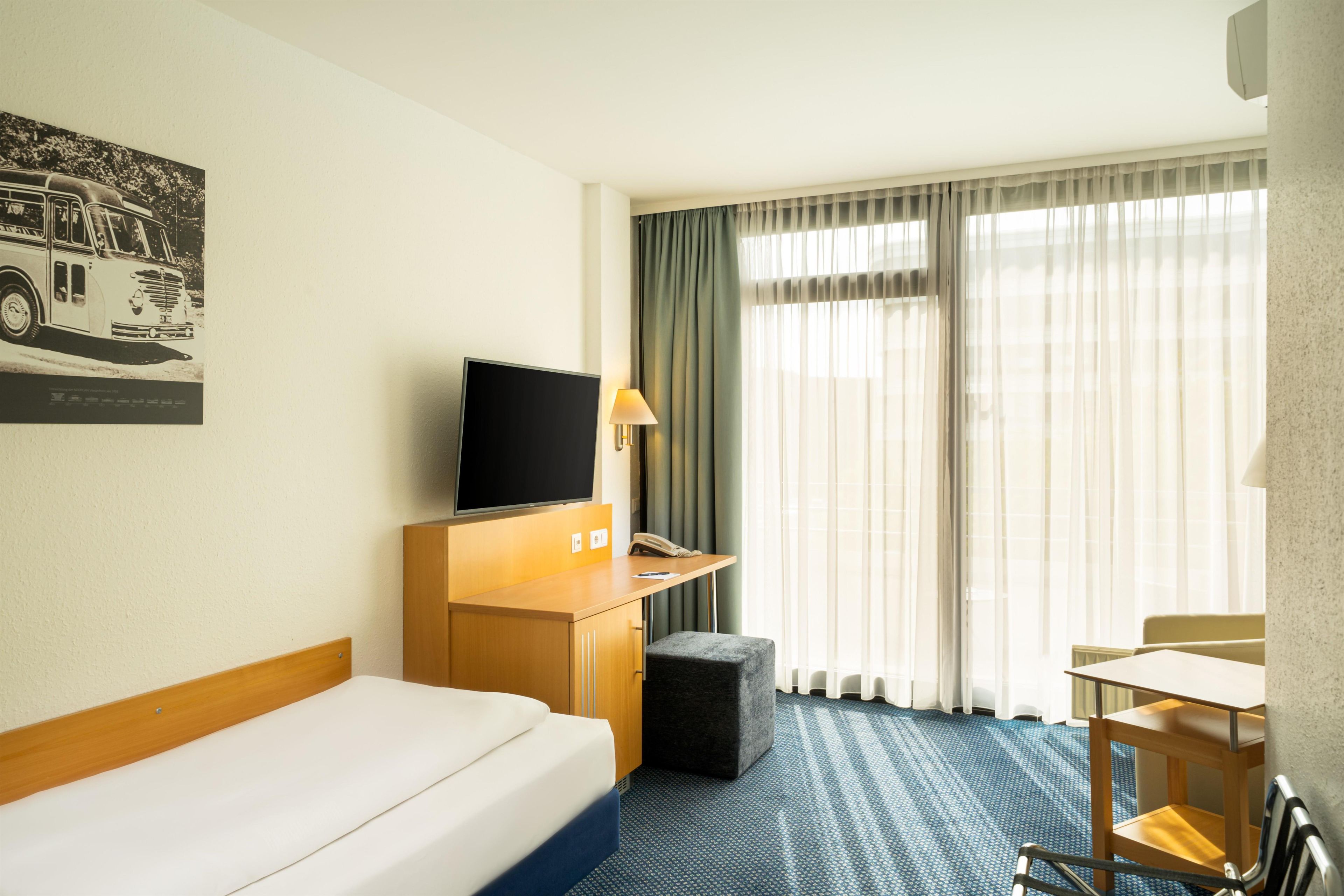 A hotel room with a bed, a desk, a television, a chair, and a window with curtains.