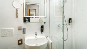 Un baño moderno con cabina de ducha de vidrio, lavamanos blanco, espejo y dispensador de jabón.