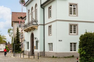En toetages bygning med en lys facade, en balkon og en brostensbelagt gade.