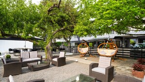 Un área de estar al aire libre con muebles de mimbre, una mesa de vidrio y un árbol que da sombra.