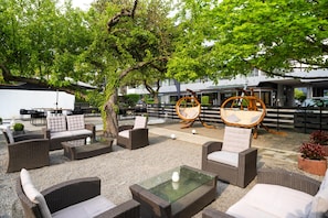 Un área de estar al aire libre con muebles de mimbre, una mesa de vidrio y un árbol que da sombra.
