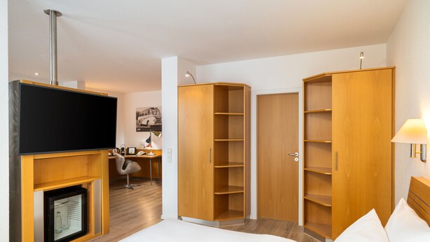 Una habitación de hotel con cama, televisión, armarios de madera, escritorio y silla.