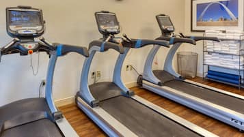 Three treadmills with digital screens, a clock on the wall, and a towel rack with folded towels.