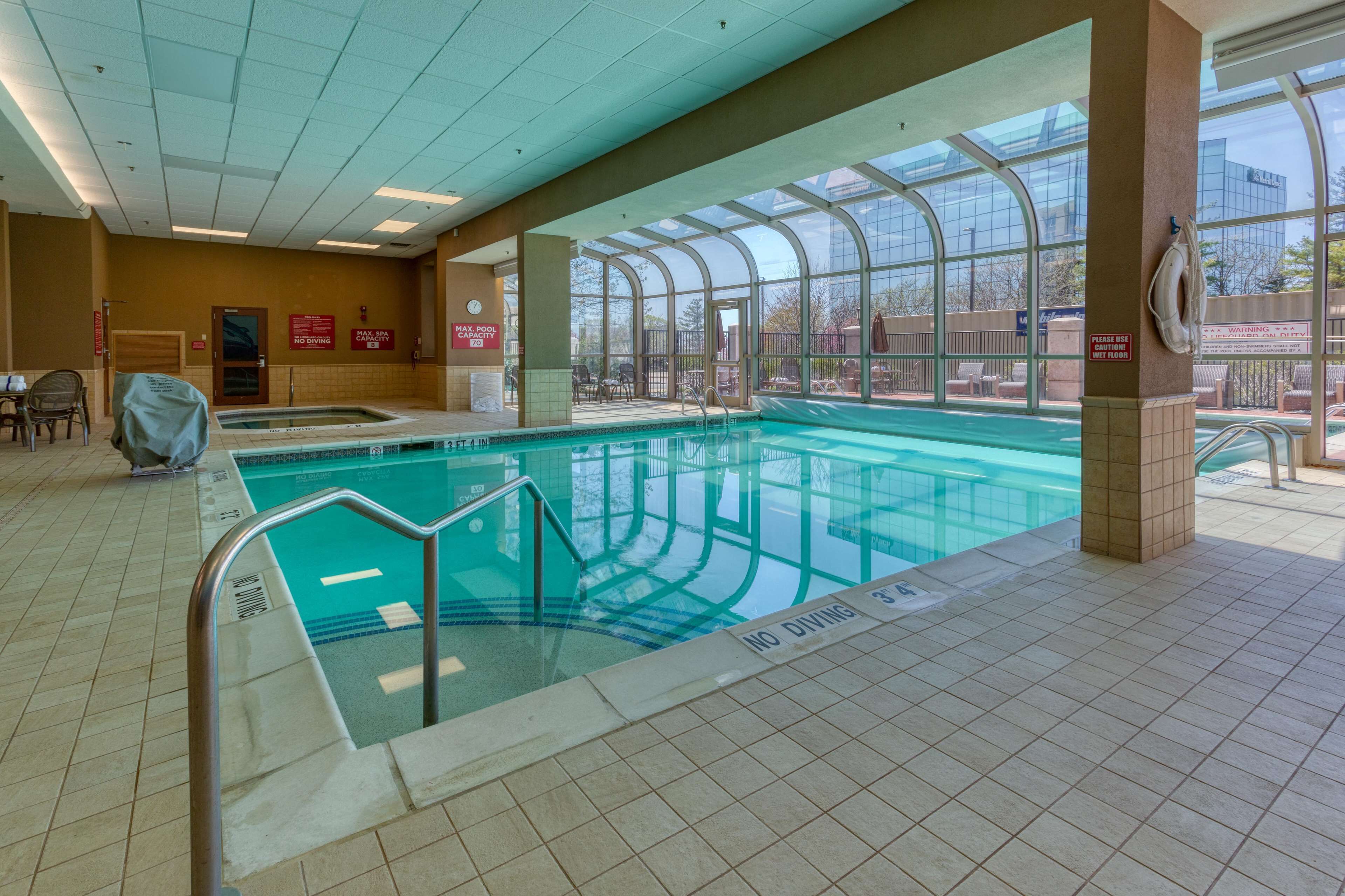 Une piscine intérieure avec des parois en verre transparent, un panneau indiquant qu’il est interdit de plonger et un poste de surveillance pour le sauveteur.
