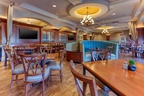 Un restaurant spacieux avec des tables et des chaises en bois, un grand écran de télévision et un lustre moderne.