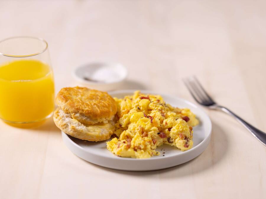A plate of scrambled eggs with sausage, a biscuit, and a glass of orange juice on a white plate.