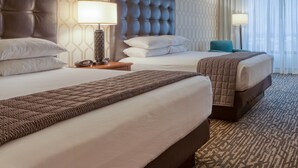 Habitación de hotel con dos camas, pared con diseño y vista a la ciudad a través de cortinas translúcidas.