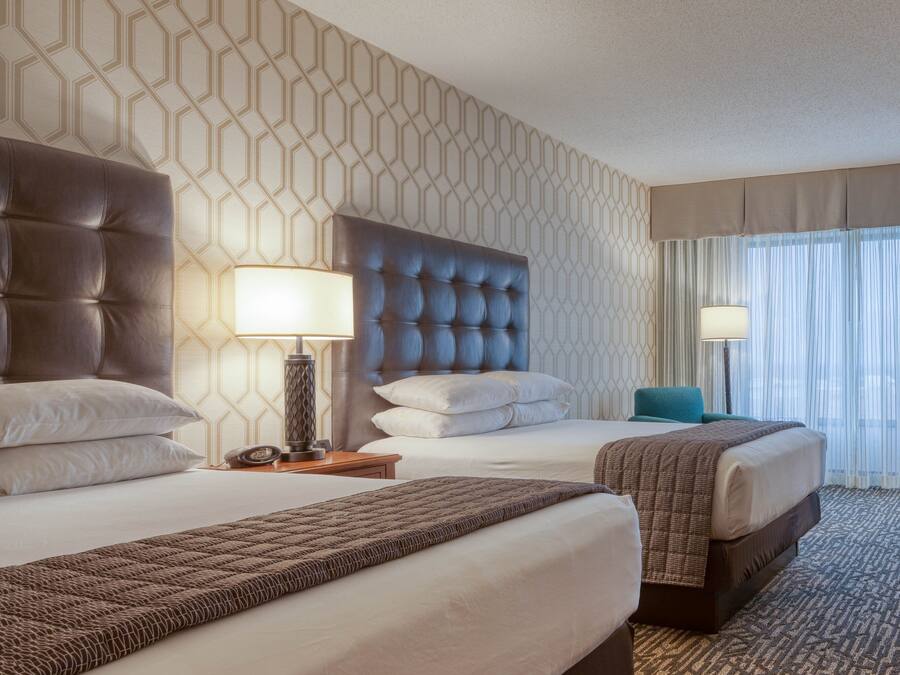 Ein Hotelzimmer mit zwei Betten, einer strukturierten Wand und Blick auf die Stadt durch leichte Vorhänge.