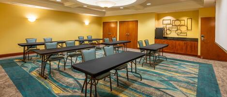 A conference room with a large table and chairs, a kitchenette, and a carpeted floor.
