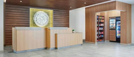 A reception area with a wooden reception desk, a wall-mounted decorative piece, and a vending machine stocked with snacks and beverages.