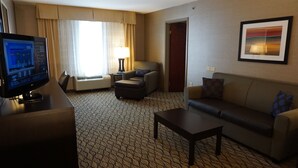 A hotel room with a TV, a sofa, a coffee table, an air conditioning unit, and a framed picture on the wall. - Fairfield by Marriott Inn & Suites New Milford (New Milford)