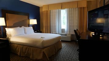 A hotel room with a large bed, a desk with a chair, a television, and a window with curtains.