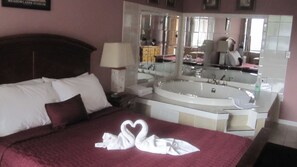 A hotel room with a bed, a large mirror, a bathtub, and a vanity with a sink. - Ritz Inn Niagara (Niagara Falls)