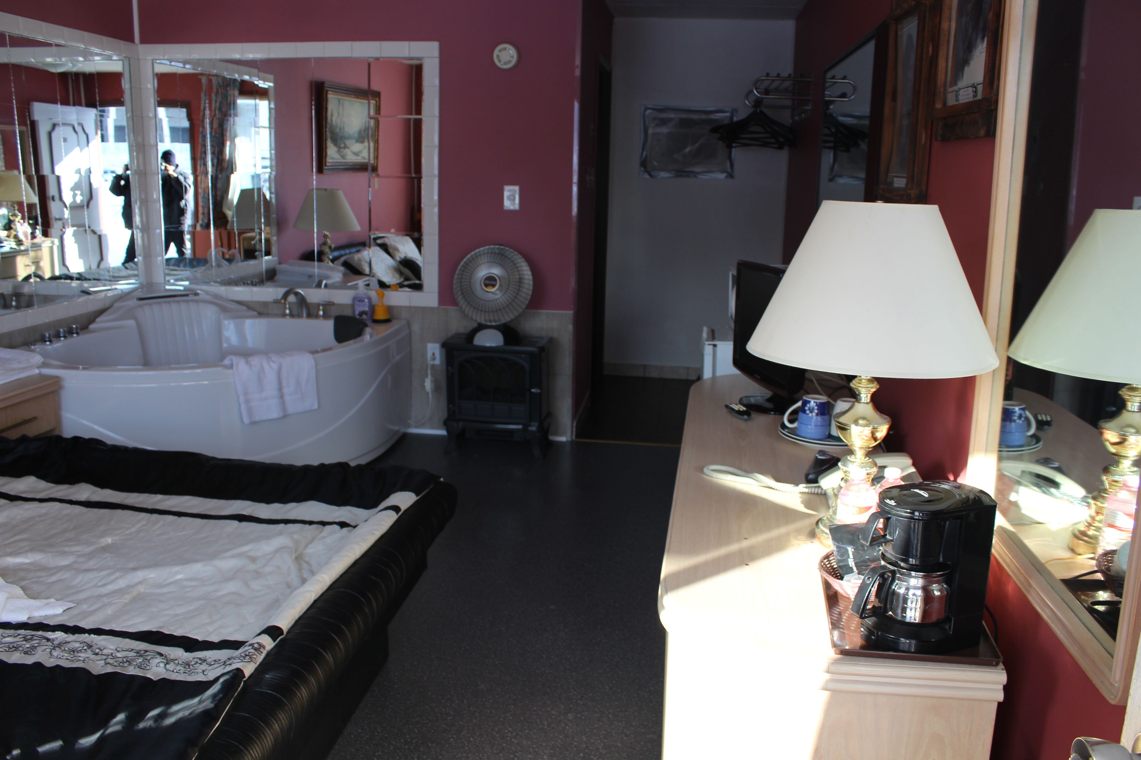 A hotel room with a large bathtub, a desk with a lamp, a coffee maker, and a mirror.
