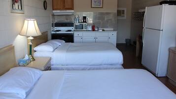 A hotel room with two beds, a nightstand with a lamp, a kitchenette with a stove, microwave, and refrigerator.