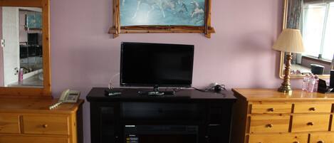 Habitación de hotel con televisión sobre un mueble de madera, un cuadro de caballos en la pared, un aparador de madera y un espejo.
