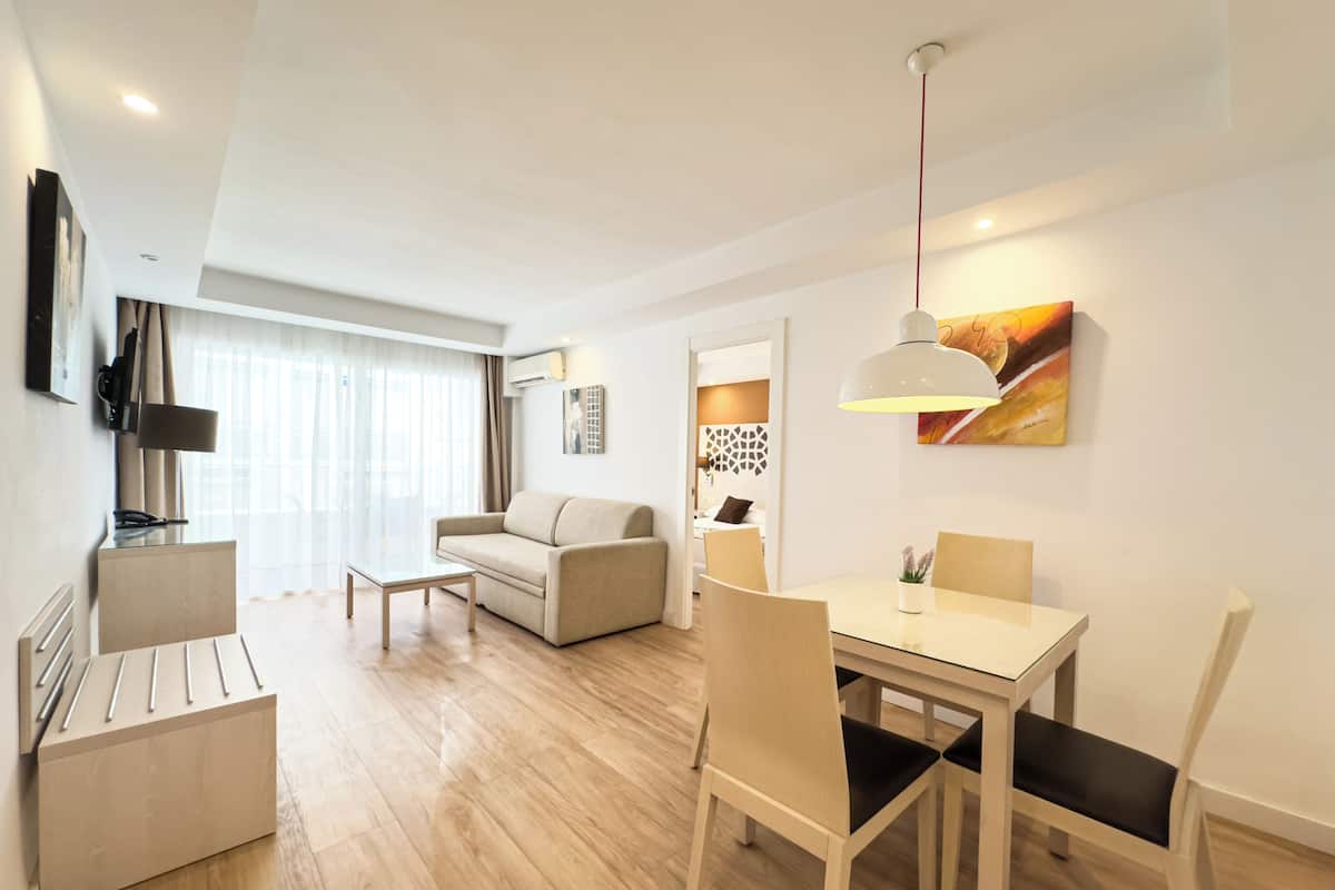 A modern hotel room with a dining area, a sofa, a coffee table, and a TV.