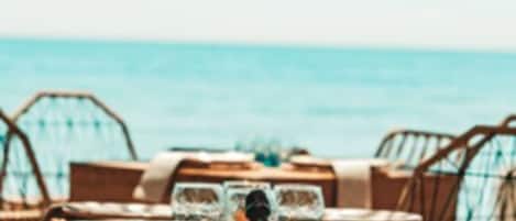A beachside dining area with wooden tables and wicker chairs, overlooking the sea.