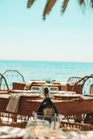 Een eetgedeelte aan het strand met houten tafels en rieten stoelen, met uitzicht op de zee.