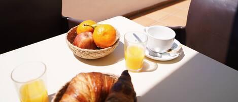 A table with breakfast items, a glass of orange juice, and a croissant on a balcony overlooking the ocean.