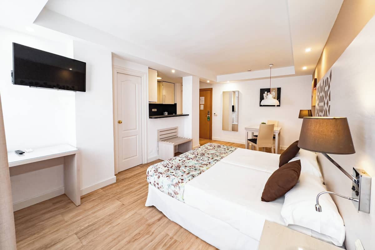 A hotel room with a bed, desk, TV, kitchenette, and a bathroom with a shower.