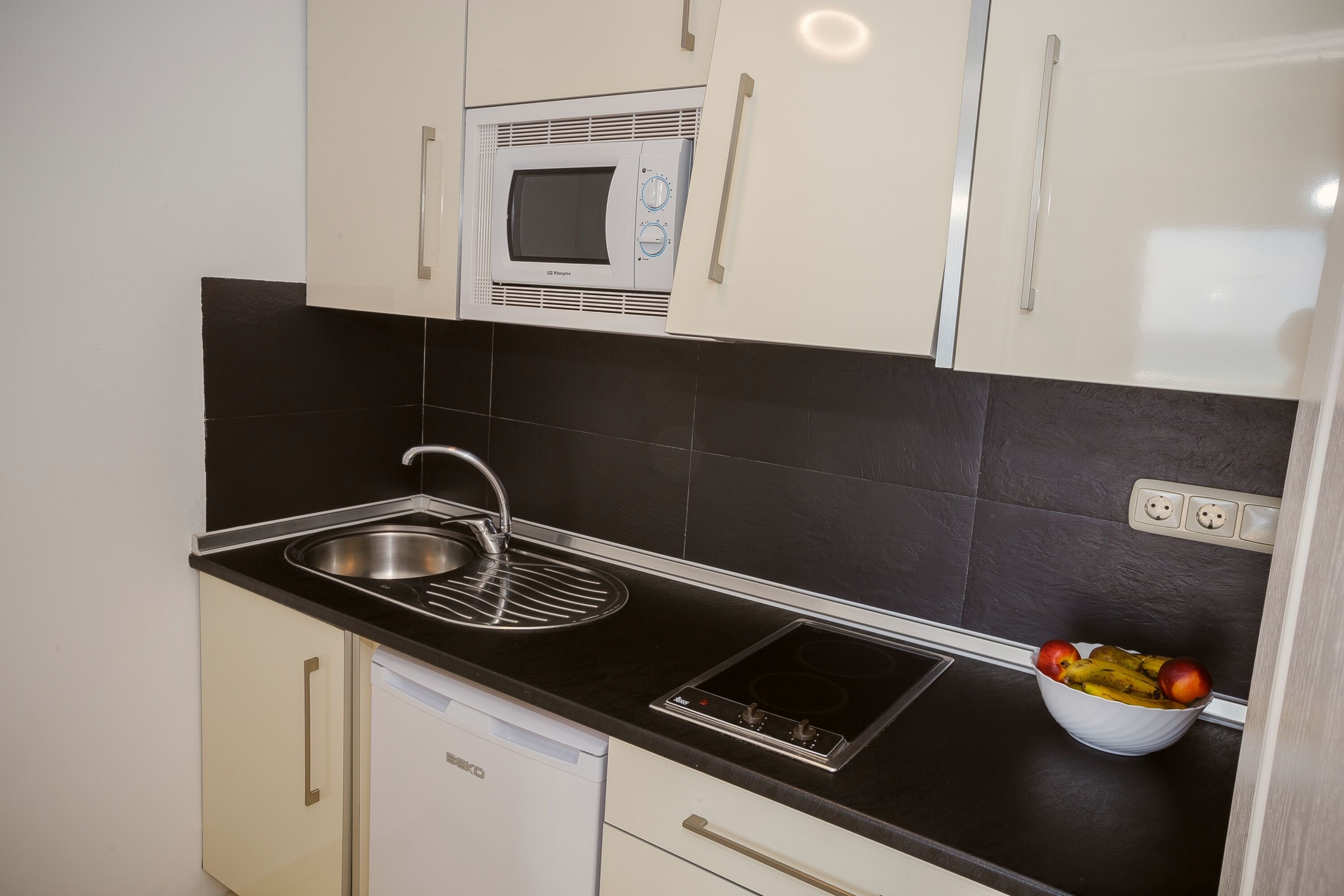 A kitchen with a microwave, sink, and a bowl of fruit.