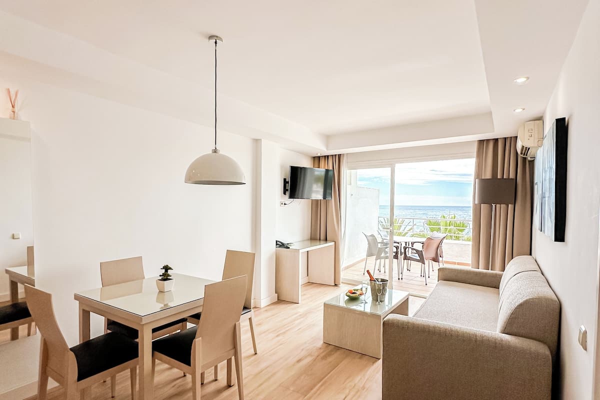 A modern living room with a dining area, a sofa, a TV, and a balcony with a view.
