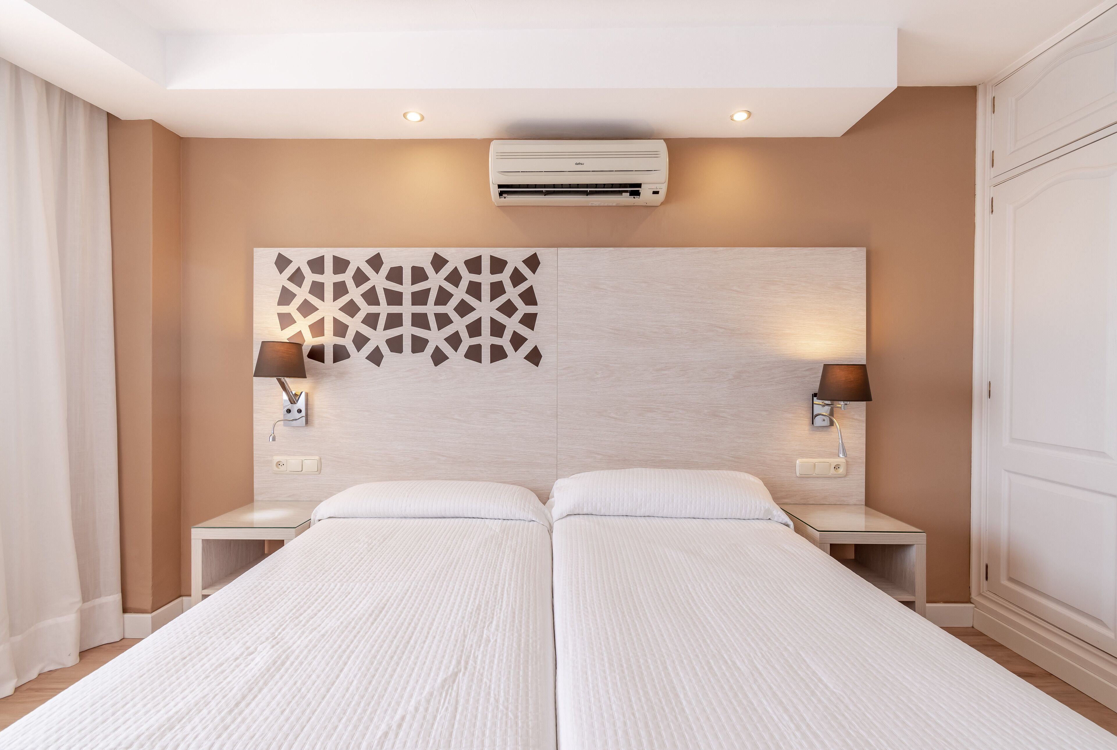 Habitación de hotel con cama doble, dos mesitas de noche, aire acondicionado de pared y un panel decorativo.