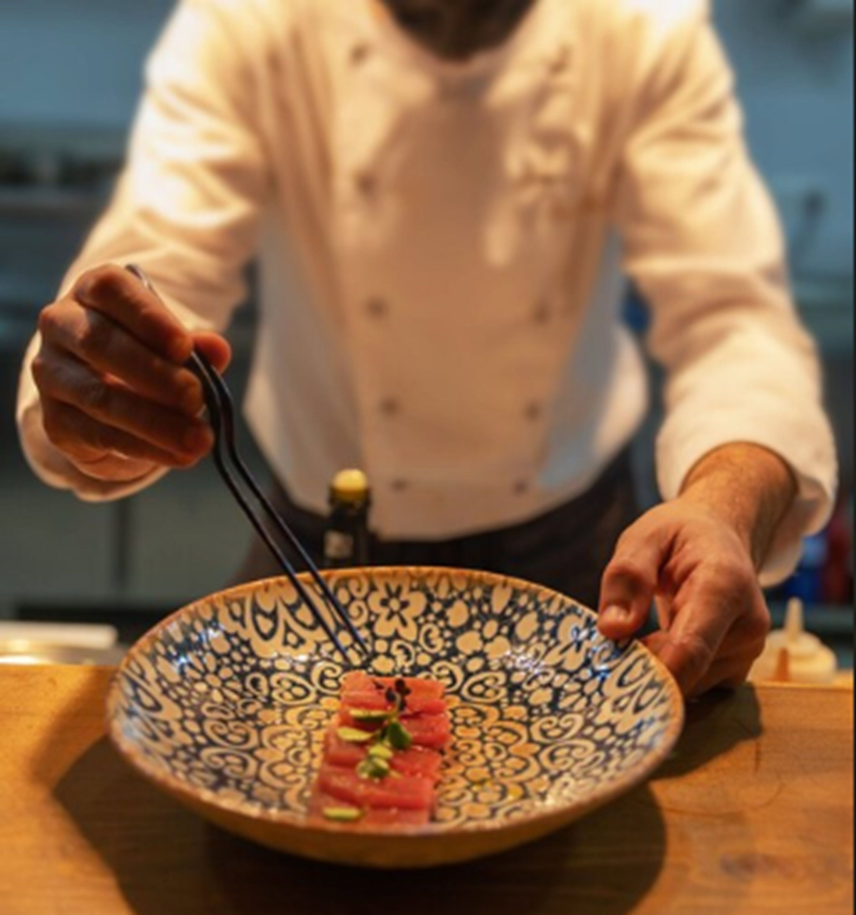 Um chef segurando hashis sobre um prato com um desenho padronizado.