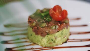 A dish with avocado, salmon, and cherry tomatoes on a white plate with brown sauce drizzles.