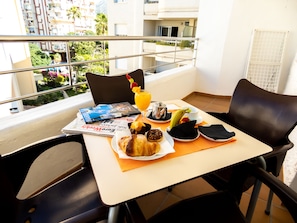 A balcony table with breakfast items, a magazine, and a view of buildings and greenery. - Puerto Azul Marbella (Marbella)