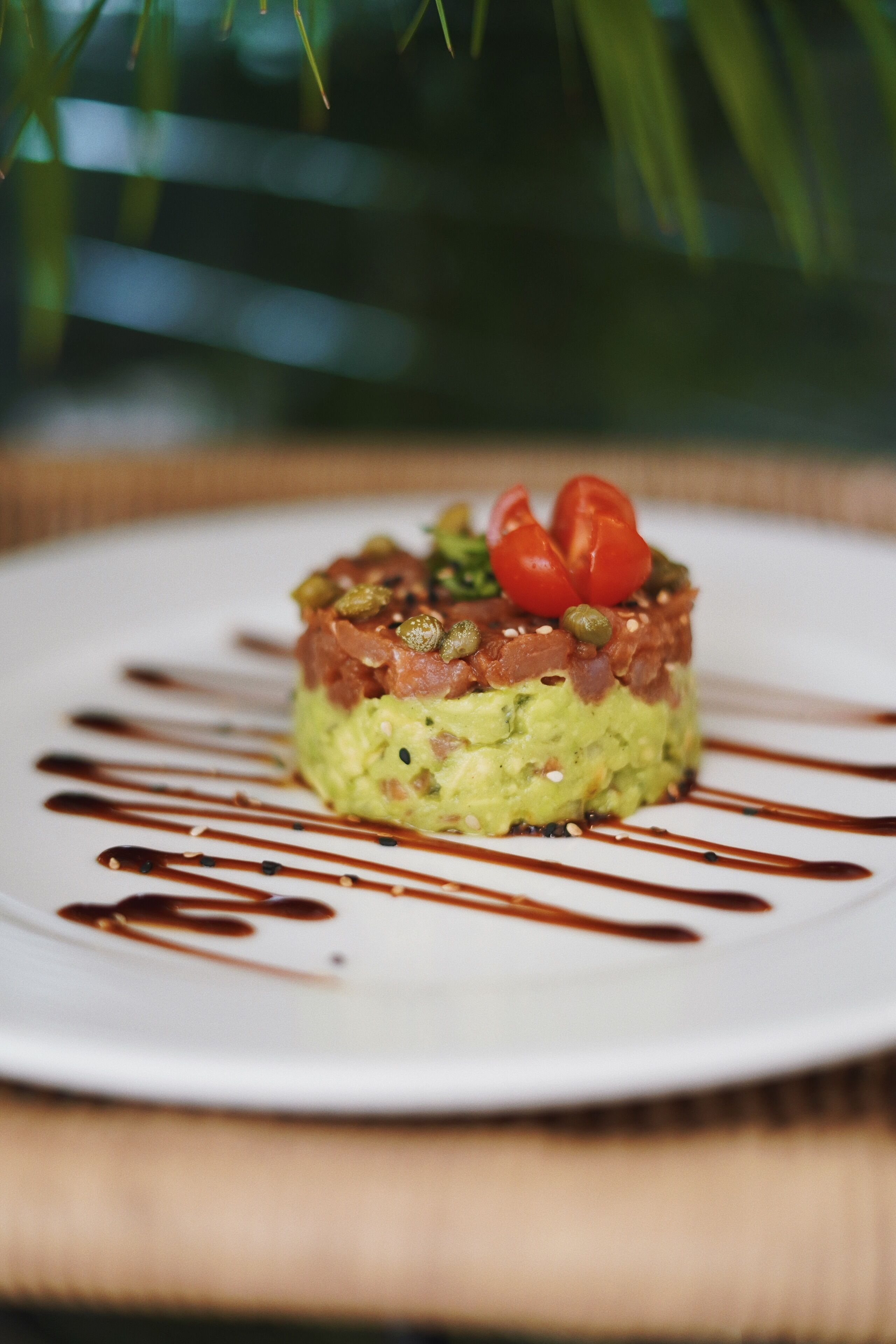 Un plat composé d’avocat, de tomates et de poivrons verts, servi dans une assiette blanche et nappé d’une sauce brune.