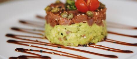 Un plat composé d’avocat, de tomates et de poivrons verts, servi dans une assiette blanche et nappé d’une sauce brune.