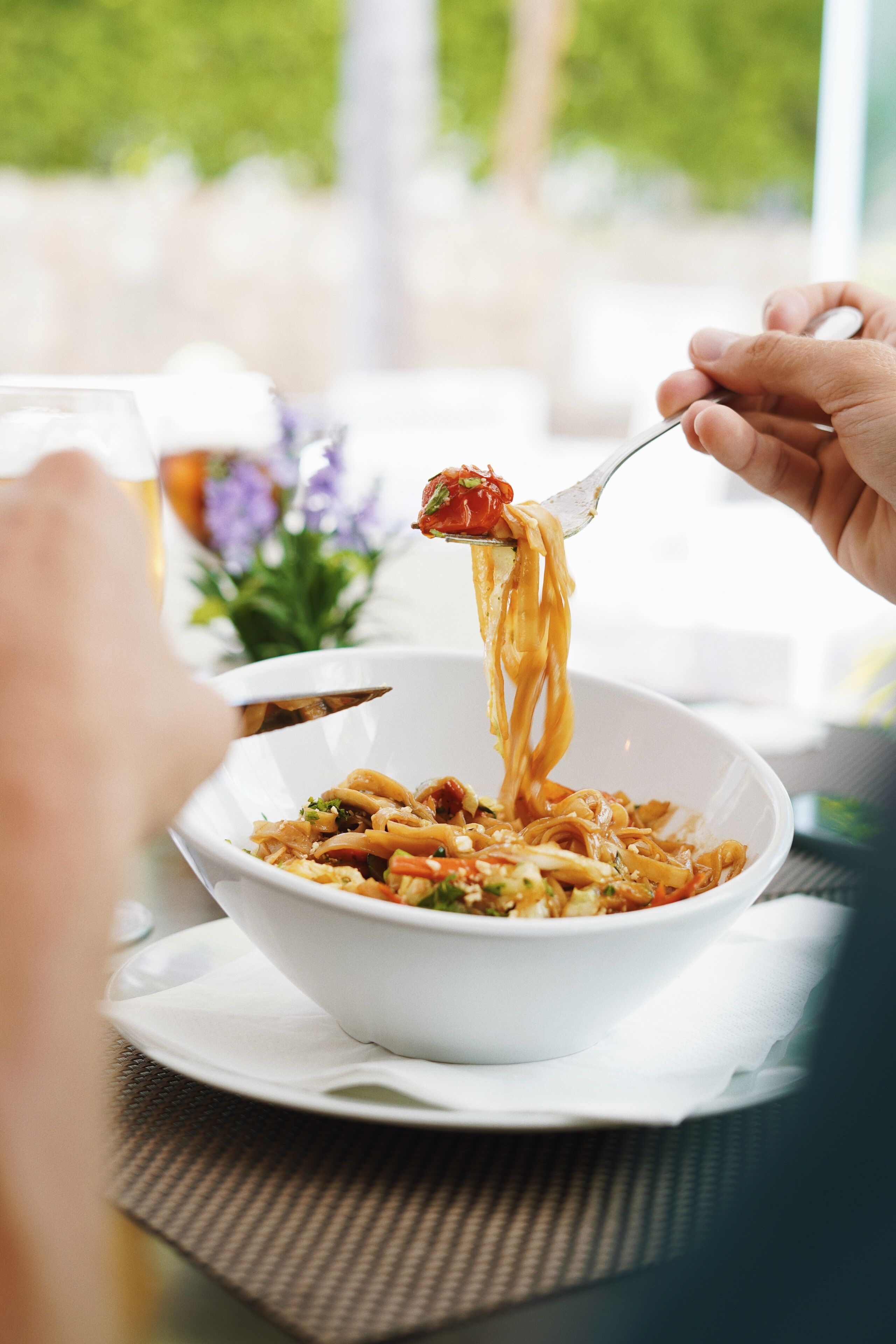 Een kom pasta met een vork die noedels optilt, geplaatst op een wit bord met een servet eronder.
