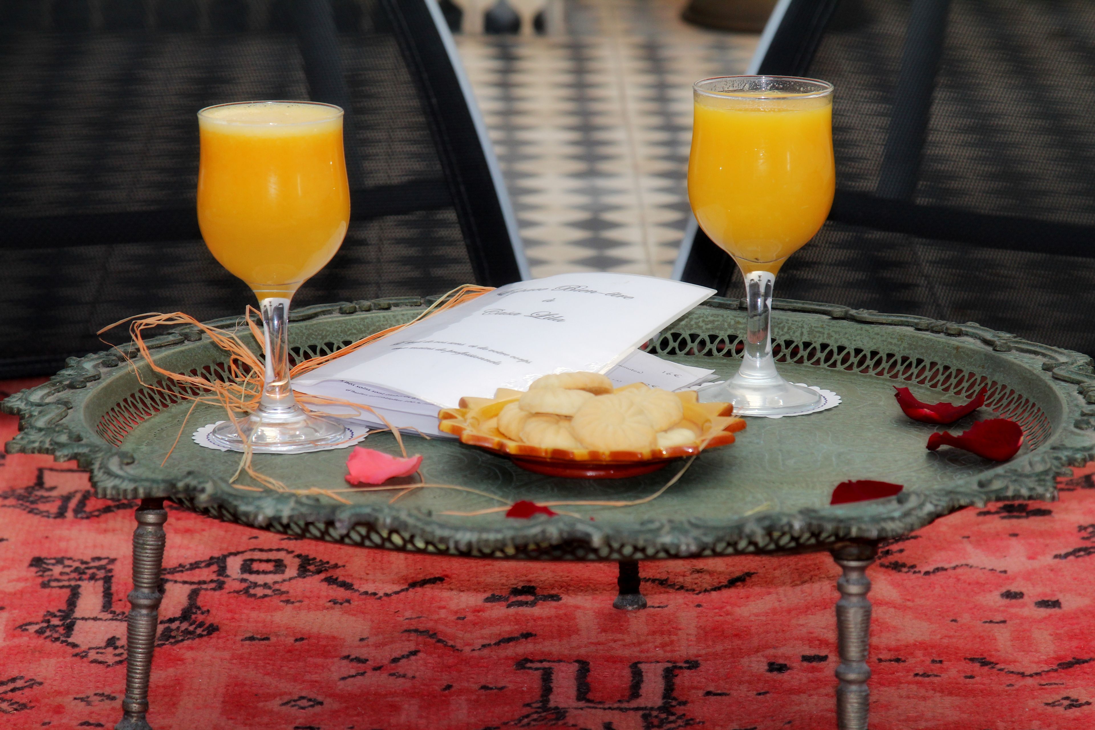 A table with two glasses of orange juice, a plate of cookies, and a menu on a green tray.